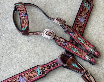 May include: A brown leather horse bridle and breast collar set featuring intricate floral tooling, leopard print accents, and inlaid purple stars and turquoise lightning bolts. The tack includes silver-toned metal buckles and hardware.