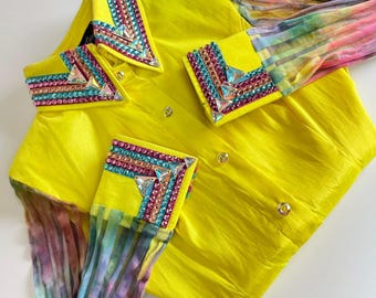 May include: A bright yellow shirt with embellished collar and cuffs. The collar and cuffs are adorned with colorful rhinestones. The sleeves are a sheer, tie-dye fabric in shades of pink, purple, and blue. The shirt has gold buttons.