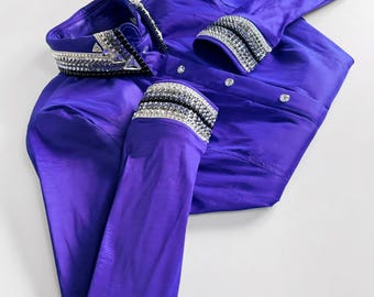 May include: A long-sleeved, vibrant purple button-down shirt featuring a structured collar and cuffs heavily embellished with rows of clear and black crystals. The shirt has a smooth, slightly lustrous finish and clear buttons down the front placket.