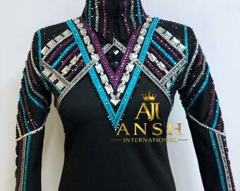 May include: A black long-sleeve shirt featuring a high collar and a V-shaped pattern on the chest adorned with turquoise, purple, and clear crystals. The text AJI ANSH INTERNATIONAL with a crown icon is printed in gold on the front of the shirt.