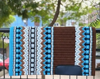 May include: A rectangular horse saddle pad featuring a brown, light blue, and white geometric pattern. The pad has a solid brown section on the right side with a dark blue leather-like patch at the bottom corner and a solid light blue border.