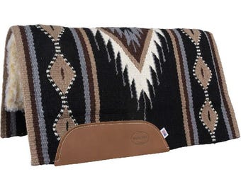 May include: A rectangular horse saddle pad featuring a black, tan, grey, and white geometric pattern. The pad has a thick, cream-colored fleece lining on the underside and a tan leather wear patch on the side embossed with the text WOOL PAD.