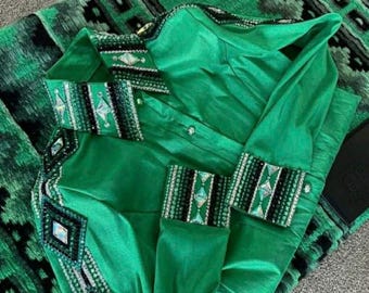 May include: A bright green long-sleeve shirt featuring a button-down front and a pointed collar. The collar, cuffs, and front panels are decorated with intricate black and silver beadwork and large, clear diamond-shaped crystals in a geometric pattern.