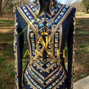 May include: A dark navy blue long-sleeve show shirt featuring a high collar, adorned with numerous iridescent square crystals, gold metallic trim, and small rhinestones. The text AJ ANSH INTERNATIONAL with a crown icon is centered on the front.