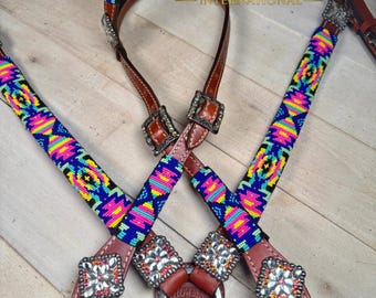 May include: A brown leather horse bridle featuring vibrant, multi-colored beaded patterns in neon pink, yellow, blue, and green. The bridle includes silver-toned metal buckles, square decorative conchos with clear crystals, and a metal bit.