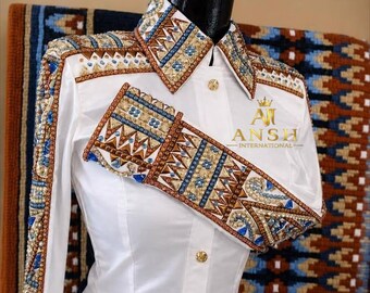May include: A white long-sleeve button-down shirt featuring intricate embroidery and beadwork in shades of blue, gold, and brown along the collar, shoulders, and cuffs. The shirt displays the gold text AJ ANSH INTERNATIONAL on the chest.