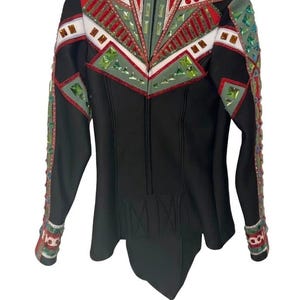 May include: Black jacket with decorative embellishments. The jacket features a high collar, a zipper closure, and a peplum hem. The shoulders and upper chest are adorned with red, green, and white geometric designs. The sleeves are also decorated with colorful accents.