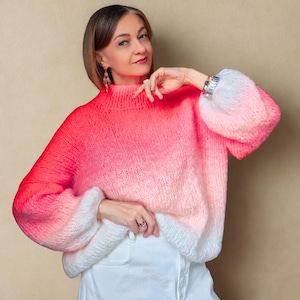 Könnte beinhalten: Ein handgestrickter Pullover mit hohem Kragen und langen, voluminösen Ärmeln. Der Pullover hat einen Farbverlauf, der von einem leuchtenden Rot oben nach einem weichen Weiß unten übergeht. Die Ärmel sind im Puffstil gehalten.