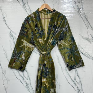 Puede incluir: Bata de terciopelo verde oliva con estampado de animales de la jungla con leopardos, tucanes y cebras. La bata tiene mangas largas y cinturón anudado. El forro interior tiene un estampado de rayas.