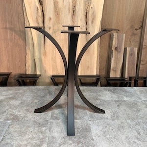 May include: A black metal table base with a central vertical support and curved legs. The base has four flat platforms for attaching a tabletop. The design is modern and minimalist, suitable for various table sizes.