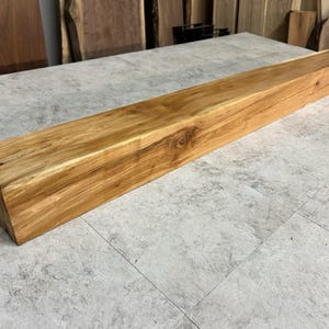May include: A rectangular, unfinished wooden beam with a natural, light brown color. The wood grain is visible, and the beam appears to be freshly cut. The beam is approximately 60 inches long and suitable for various woodworking projects.