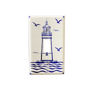 May include: White ceramic light switch cover with a blue lighthouse design and seagulls flying above the waves.