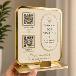 May include: A rectangular sign with a gold frame and white background featuring two QR codes for Instagram and a website. The text reads Thank You For Visiting, We Appreciate Your Support, Stay Connected, and We're Glad You're Here with gold accents.