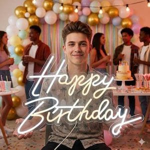 Può includere: Un'insegna al neon con la scritta "Happy Birthday" in corsivo, tenuta da una persona. L'insegna è bianca e gialla. Lo sfondo comprende palloncini, una torta e diverse persone a una festa.