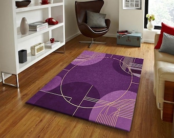 May include: A rectangular purple area rug with a geometric design featuring circles and lines in shades of purple and gold. The rug is placed on a hardwood floor, adding a touch of color to the room.