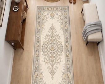 May include: An overhead shot of a rectangular rug with an ornate floral design in cream, beige, and blue tones. The rug is placed in a hallway with wooden flooring, a wooden console table, and a bench.