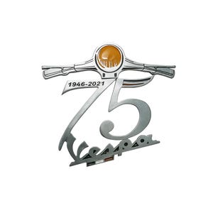 Puede incluir: Un emblema plateado del 75 aniversario de Vespa. El emblema presenta el logotipo de Vespa, el número 75 y los años 1946-2021. El emblema tiene un acabado plateado con un acento naranja y negro.