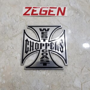 以下が含まれることがあります： 黒い文字でWest Coast Choppersと書かれた鉄十字型の銀と黒の金属製エンブレム。エンブレムの上には、赤い文字でZ E G E Nと印刷された別の白い長方形のステッカーがあります。