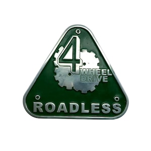 Peut inclure: Un emblème métallique vert et argenté avec les mots "4 WHEEL DRIVE ROADLESS". L'emblème est triangulaire avec une bordure argentée et un design d'engrenage.