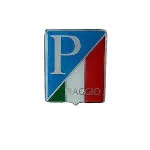 Pode incluir: Um pin quadrado da Piaggio com fundo azul e um "P" branco. O design incorpora as cores da bandeira italiana: verde, branco e vermelho. A palavra "PIAGGIO" está impressa em branco na parte inferior.