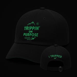 Peut inclure: Casquette de baseball noire avec une visière incurvée et une sangle réglable. Le devant affiche le texte "Trippin' on Purpose" en vert, avec un motif de montagne et d'avion. Le dos de la casquette porte l'inscription "I Tripped" en vert.