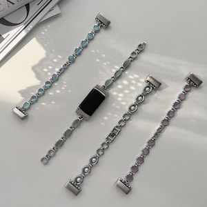 May include: Four silver-toned watch bands with decorative stone accents. One band has a black rectangular watch face. The other bands feature light blue, green, and pink stones. The bands are displayed on a white surface.