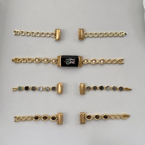 Op de afbeelding: Goudkleurige horlogebandjes met verschillende ontwerpen. Eén bandje heeft een zwart scherm met de tekst "01 27". Andere bandjes hebben parel- en edelsteenaccenten. De bandjes liggen op een witte ondergrond.