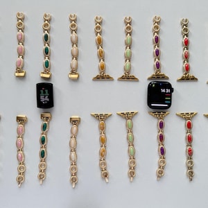 Könnte beinhalten: Gezeigt werden goldfarbene Uhrenarmbänder mit verschiedenen Edelsteinakzenten, darunter Grün, Rosa und Lila. Zwei Smartwatches sind ebenfalls vorhanden, eine mit schwarzem Bildschirm, der die Uhrzeit anzeigt.