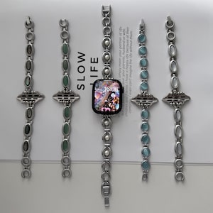 May include: Five silver-toned watch bands with decorative stone accents. The center band features a smart watch displaying the time 16:06. The bands have various stone colors, including green, blue, and white.