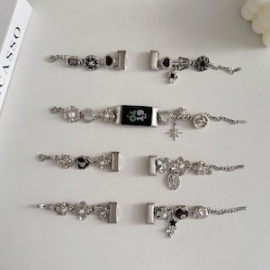 Pode incluir: Pulseiras de relógio prateadas com berloques decorativos, incluindo flores, pérolas e estrelas. Uma pulseira está presa a um mostrador de relógio digital preto. As pulseiras apresentam vários estilos de fecho e detalhes intrincados.