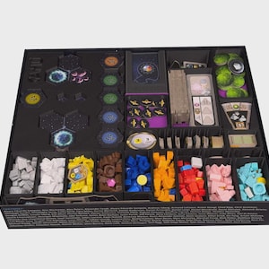 May include: A black board game organizer box containing various compartments filled with game components. It includes hexagonal tiles, stacks of cards, and small plastic tokens in colors such as white, yellow, brown, blue, orange, red, pink, and light blue.