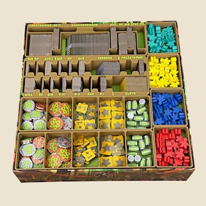 Könnte beinhalten: Ein Brettspiel-Organizer mit mehreren beigefarbenen Fächern, gefüllt mit verschiedenen Spielkomponenten, darunter Stapel grauer Karten, kleine grüne, gelbe, blaue und rote Holzfiguren, runde Atom-Muster-Plättchen sowie kleine grüne Zylinder.