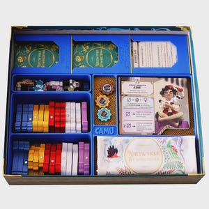 May include: A board game box organiser containing blue plastic trays filled with colourful wooden tokens in blue, yellow, red, white, and purple. The set includes decks of cards labelled Niezwykłe Stworzenia, a character card for Ashe, and a white cloth bag.