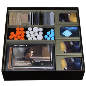 Könnte beinhalten: Eine Brettspiel-Organizer-Box mit verschiedenen Spielkomponenten, darunter Kartenstapel, orangefarbene sechseckige Spielsteine, weiße runde Spielsteine, blaue wassertropfenförmige Spielsteine und eine Charakterkarte von Paul Atreides mit polnischem Text.
