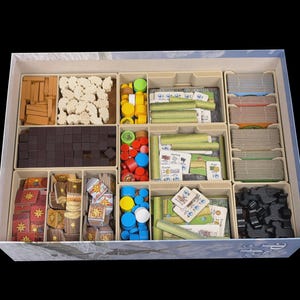 May include: A board game box organizer containing various game components including wooden cubes, tokens, cards, and shaped pieces in tan, brown, white, green, red, blue, and black, all neatly arranged in individual molded compartments.