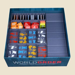 Op de afbeelding: Een bordspeldoos-organizer met grijze plastic bakjes gevuld met kleurrijke speltokens en kaarten. De voorkant van de doos bevat de tekst "WORLD ORDER" en "EDYCJA ROZSZERZONA". De binnenkant is verdeeld in secties met oranje, rode, blauwe en gele vierkante tegels met diverse iconen.