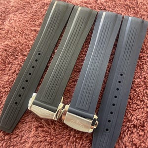 May include: Two pairs of black rubber watch straps featuring vertical ribbed textures and silver-toned metal deployment clasps engraved with the Longines brand name. Each strap includes a series of circular adjustment holes for a secure fit.