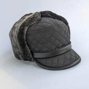 May include: A black quilted trapper hat with a faux fur lining and ear flaps. The hat has a black leather band and a short brim. The hat is designed to provide warmth and protection from the cold.