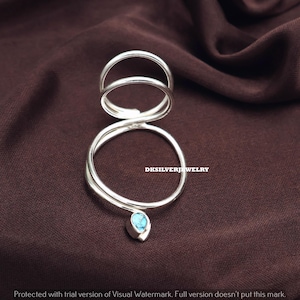 May include: A silver ring with a unique design. The ring features two upper bands and a larger lower band, connected by a swirling design. A small, light blue gemstone hangs from the bottom. The text "DKSILVERJEWELRY" is visible.