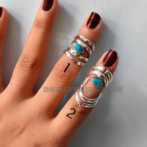 Puede incluir: Dos anillos de plata con piedras turquesas se muestran en dedos. El anillo 1 tiene un diseño en capas, mientras que el anillo 2 tiene un estilo articulado único. Los anillos se destacan sobre un fondo neutro.