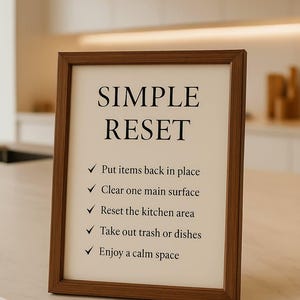 May include: A framed print with the words "SIMPLE RESET" in large black letters. Below, a list of tasks: Put items back in place, Clear one main surface, Reset the kitchen area, Take out trash or dishes, and Enjoy a calm space.