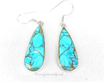 May include: A pair of teardrop-shaped earrings with a silver-colored metal frame. The earrings feature a turquoise stone with brown veining. The earrings are hanging on a white surface.