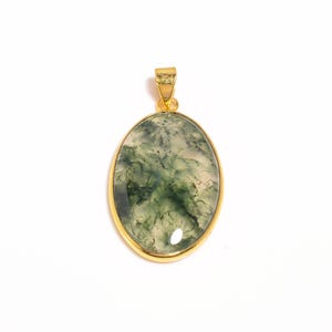May include: Oval-shaped pendant with a gold-colored frame. The pendant features a green and white stone with a unique, marbled pattern. The bail is also gold-colored. The pendant is displayed against a white background.