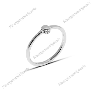 May include: A delicate silver ring featuring a small heart-shaped design. The ring has a thin band and a polished finish, reflecting light. The heart is centered on the band, creating a minimalist and elegant look. Jewelry.