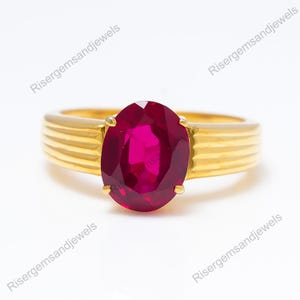 Peut inclure: Une bague en or ornée d'un grand rubis de forme ovale. La bague présente un design de bande côtelée. Le rubis est d'un rouge profond et vibrant, serti dans une monture en or. La bague est présentée sur fond blanc.