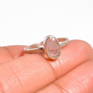 Op de afbeelding: Een zilveren ring met een peervormige, lichtroze edelsteen. De ring heeft een dunne, gepolijste band en de edelsteen is gezet in een eenvoudige bezel. De ring wordt getoond op een hand tegen een witte achtergrond.