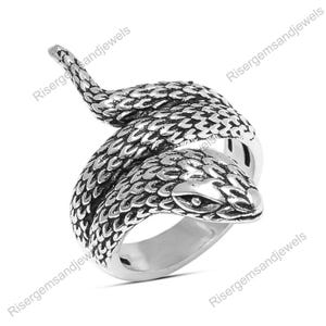 Op de afbeelding: Een zilverkleurige ring in de vorm van een slang. Het lichaam van de slang wikkelt zich om de vinger, met de kop omhoog. De ring heeft gedetailleerde schubben en een getextureerd oppervlak, waardoor het er realistisch uitziet. De ring is waarschijnlijk van metaal.