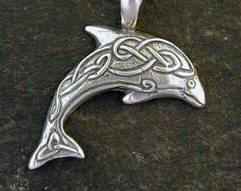 May include: A silver dolphin pendant necklace with a Celtic knot design. The pendant is hanging on a silver chain against a gray stone background.
