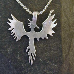 May include: A silver necklace with a detailed phoenix pendant. The phoenix is a mythical bird that symbolizes rebirth and renewal.
