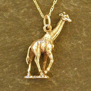 May include: A gold chain necklace with a gold giraffe pendant. The giraffe is standing on a small base.